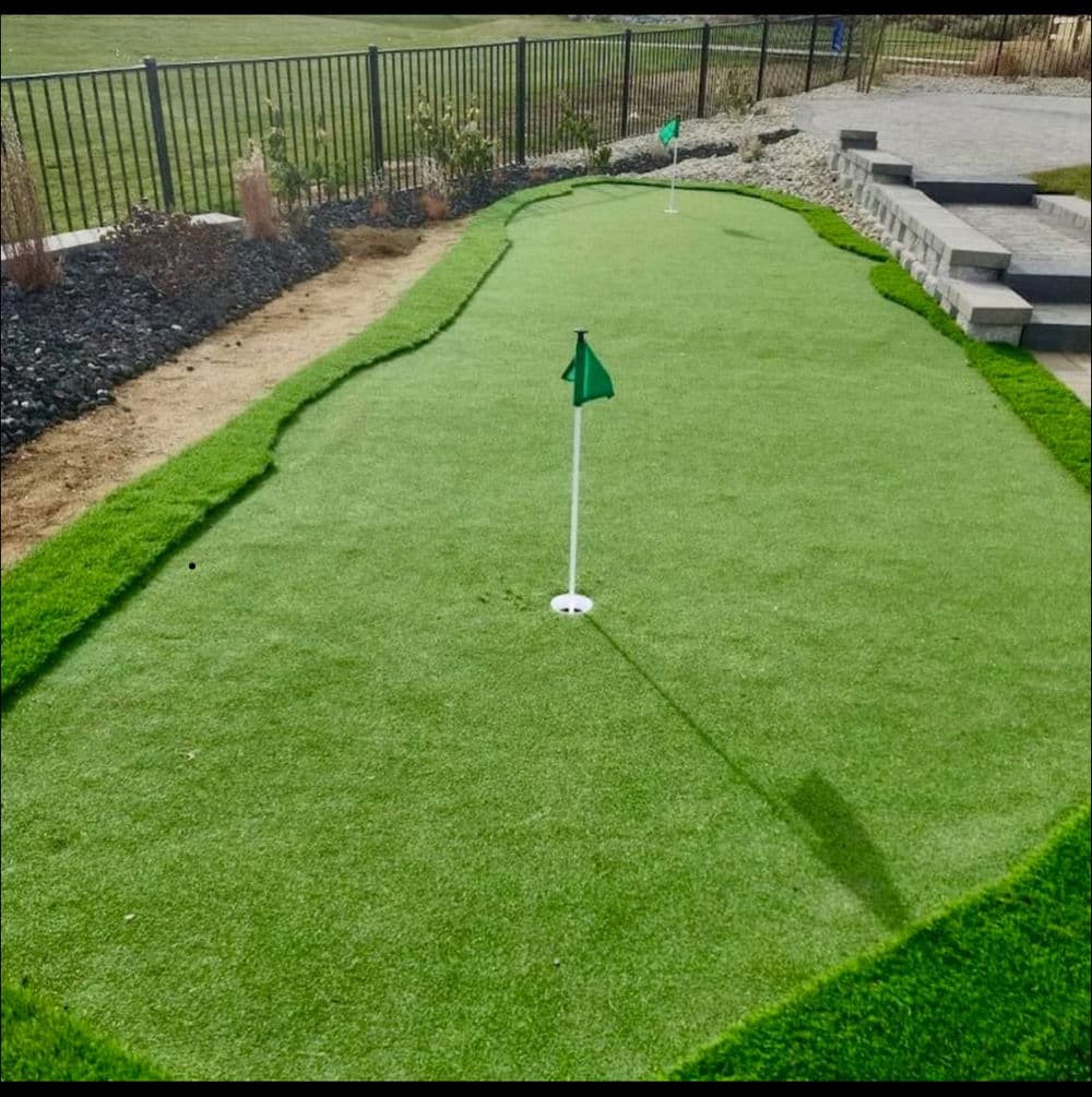 Artificial putting green with two holes and flags in a landscaped yard.