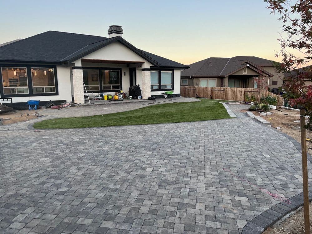 Modern house exterior with paver driveway and freshly laid sod in front yard at dusk.